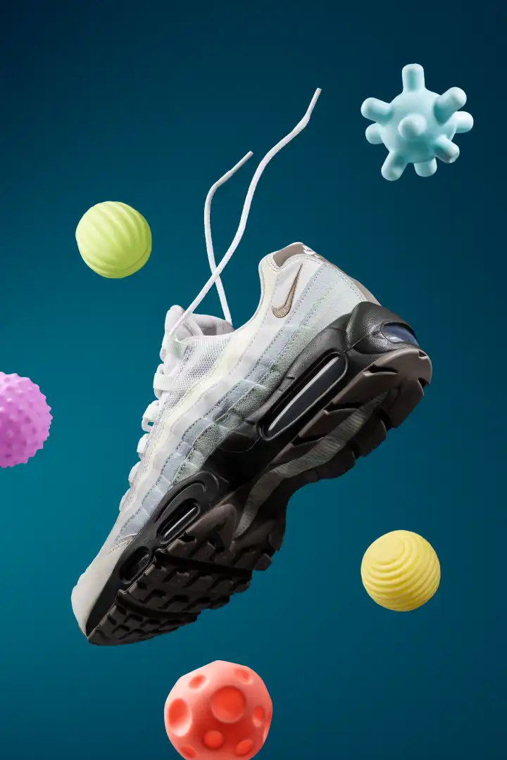 White and gray Nike sneaker with black sole floating against a teal background surrounded by colorful textured balls.