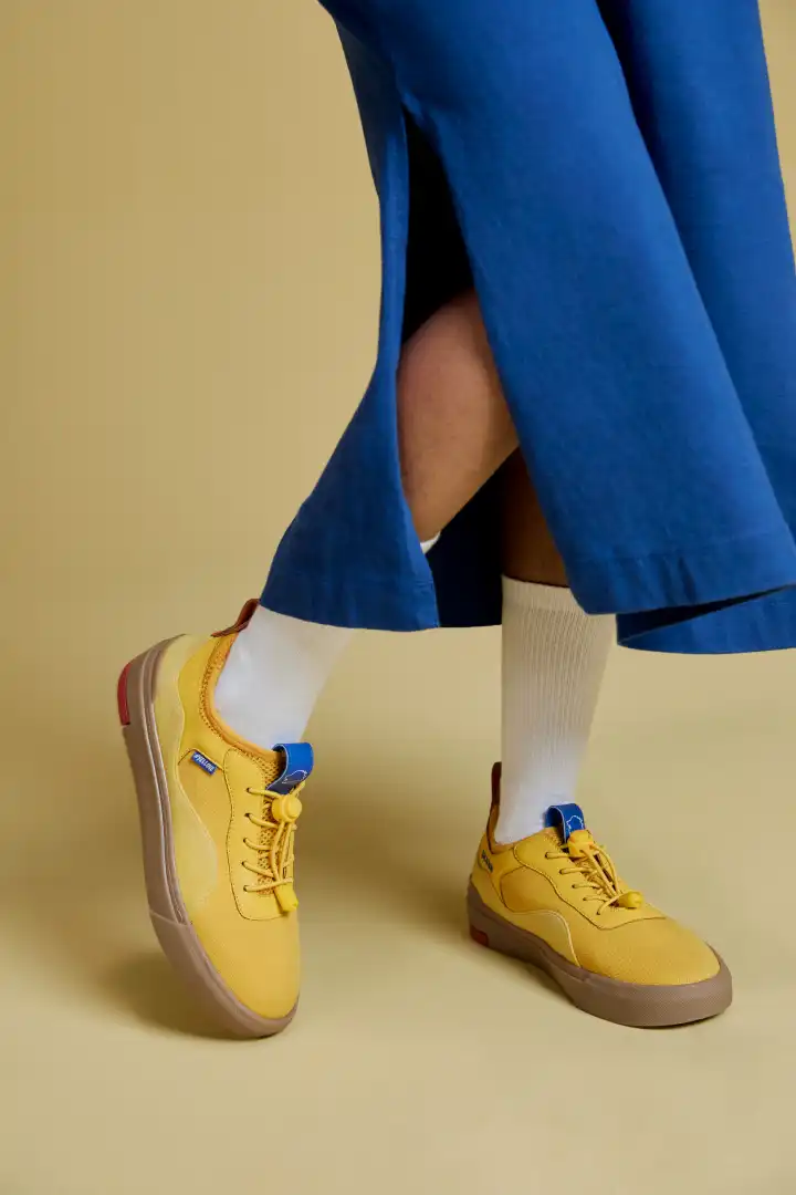 Person wearing white socks, blue wide-leg pants, and yellow sneakers with blue accents on a beige background.