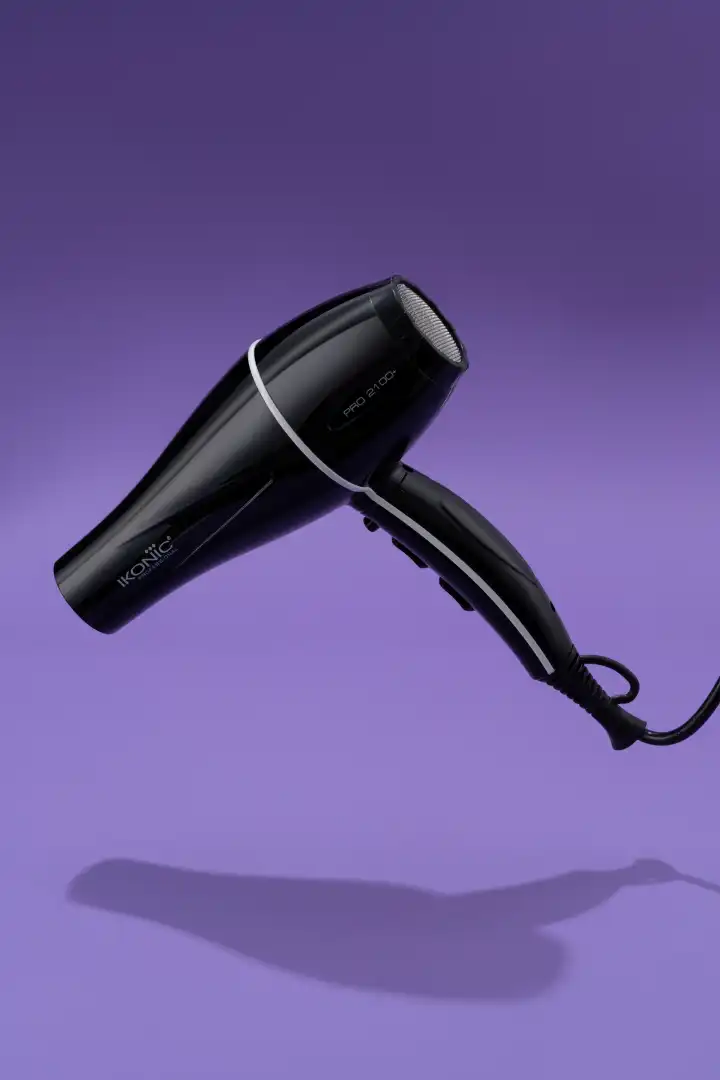 Black Ikonic Pro 2100 hair dryer with a cord against a purple background.