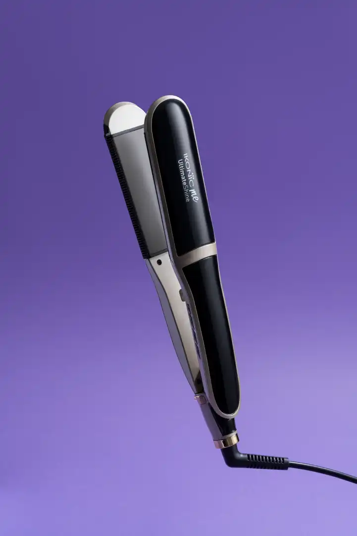 Black and silver Ikonic ME Ultimate Shine hair straightener with an attached power cord on a purple background.