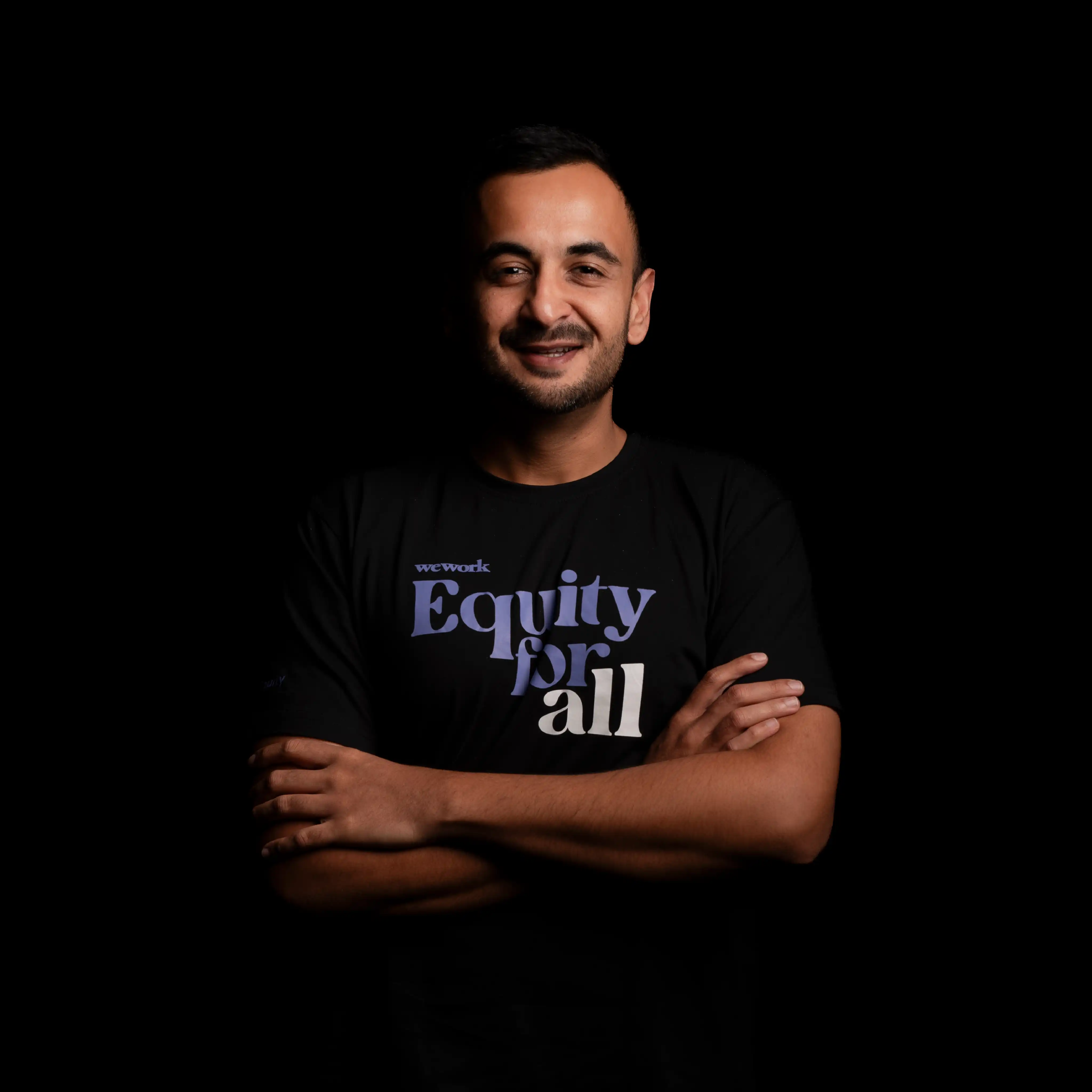 Man with short hair and beard smiling, wearing a black t-shirt with 'wework Equity for all' text on a black background.