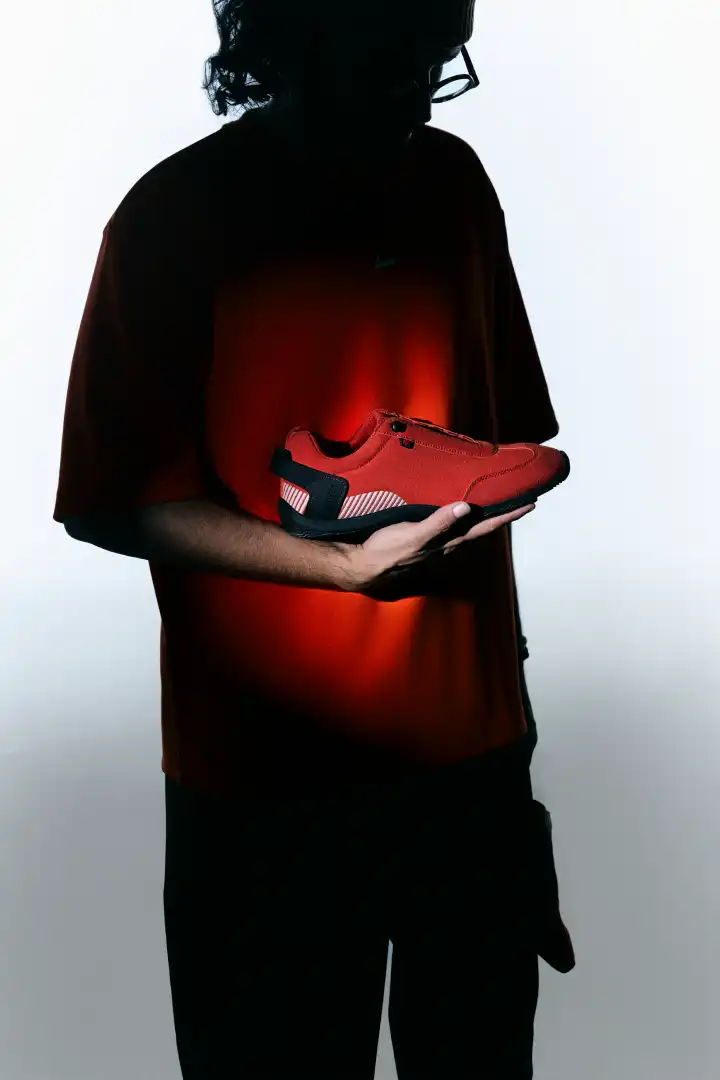 Person holding a bright red sneaker with black and white accents against a white background.