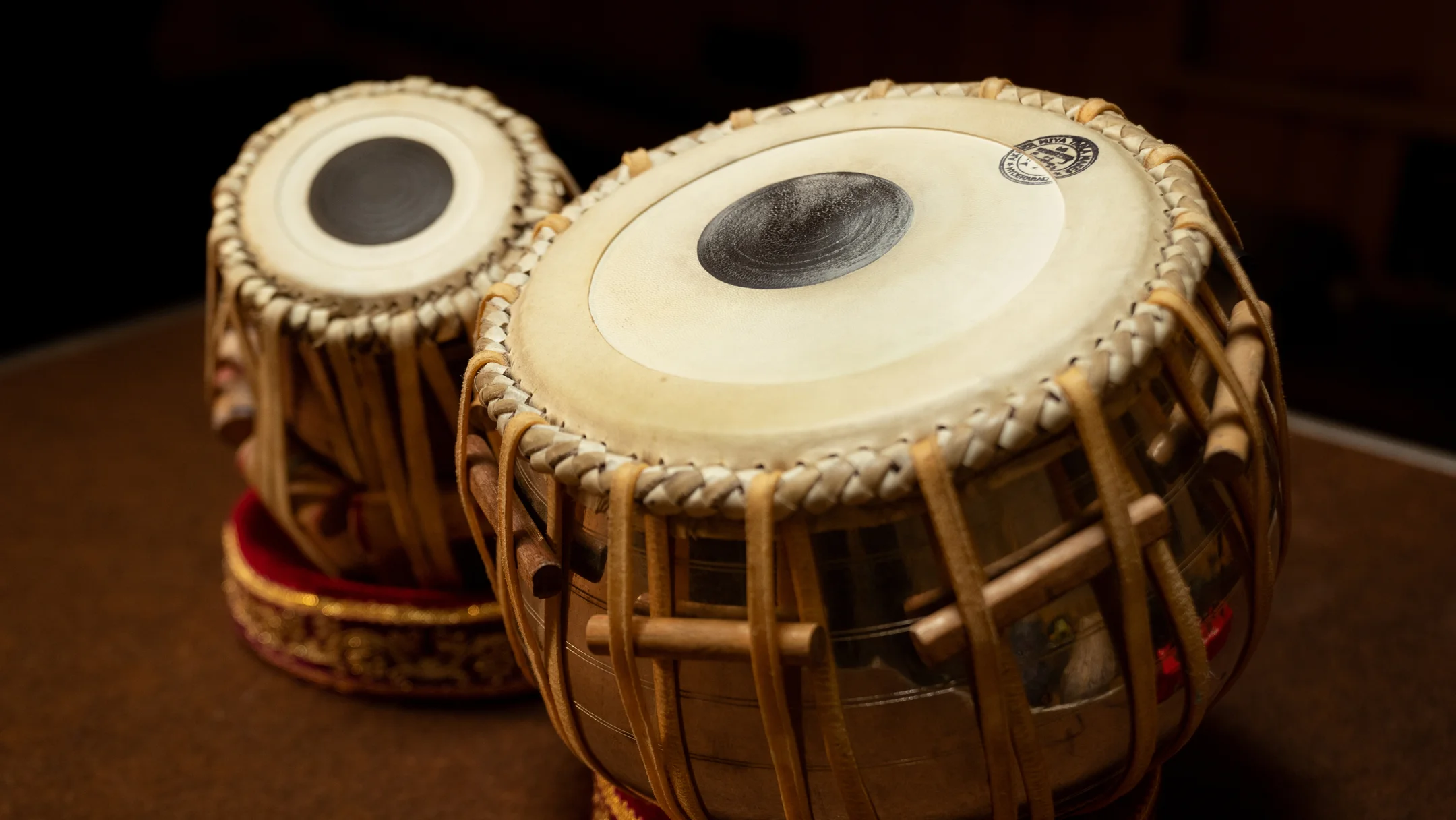 A pair of traditional Indian tabla drums with leather straps and wooden tuning pegs on a wooden surface.
